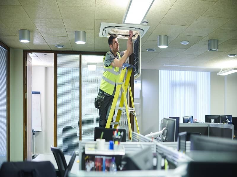 A man is fixing the light on the workspace inside the office